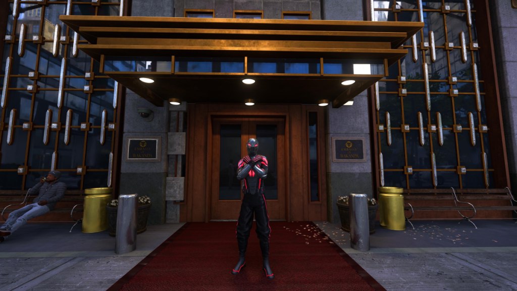 An image showing Miles Morales in front of the Wakandan Embassy doing the Wakandan salute. He's wearing his Wakanda-style suit. The picture is part of an article listing all the suits for Miles Morales in Marvel's Spider-Man 2 and how to unlock them.