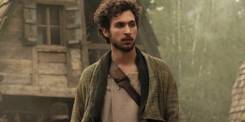 An image of actor Barney Harris as Mat Cauthon in Wheel of Time Season 1 standing amid some houses wearing a brown jacket and plain shirt as part of an article on why he was recast.