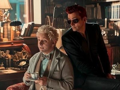 Aziraphale drinking tea in his bookshop while Crowley leans over his shoulder in a still from Good Omens 2.