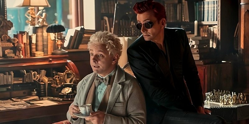 Aziraphale drinking tea in his bookshop while Crowley leans over his shoulder in a still from Good Omens 2.