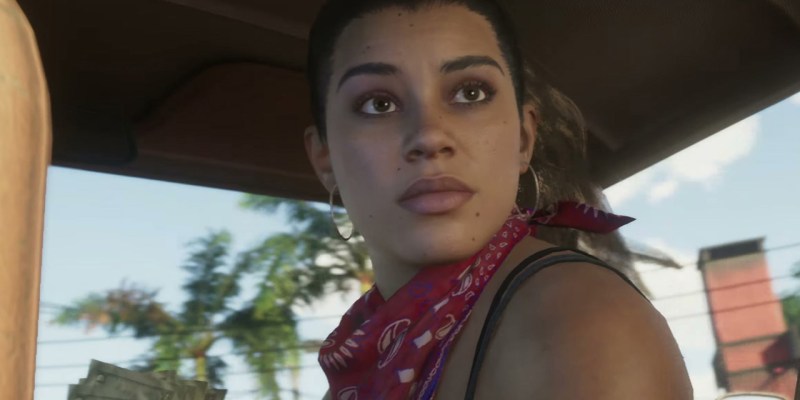 A women in a car, turning around to face the back seat, with a bandana round her neck. This image is part of an article about who voices Lucia in GTA 6.