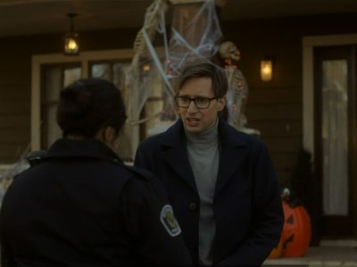 A policewoman talking to a man in glasses outside his house.