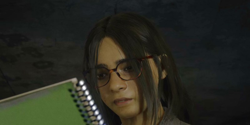 A girl with glasses and brown hair looking at a green notebook.